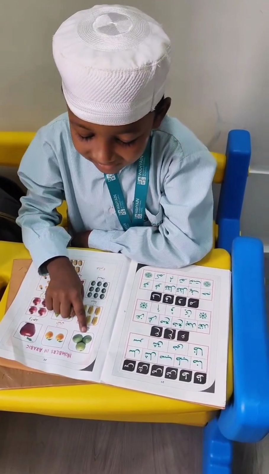 A young boy at Wahyain International School pointing at his Arabic numbers book